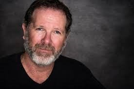 Jesser in black v-neck smiling at camera with a dark grey background