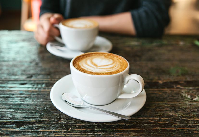 White coffee mug on a brown table with a heart design in the latte. 