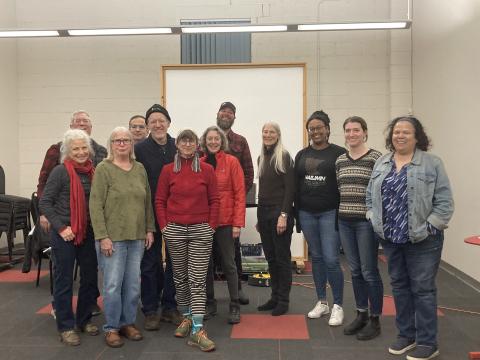 A group of smiling people, many wearing winter coats, hats and scarves pose for a photograph in a well-lit room.