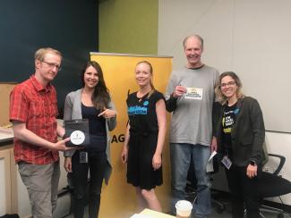 Ryan holding a black box with a SAGAFTRA magnet, Walters pointing to black box, Dornfeld smiling for the camera, O'Grady holding a "I AM A SAG-AFTRA BROADCASTER" sticker with Browning smiling next to him. 