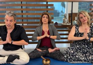 Performers in a yoga namaste pose with sound bowl in front of them