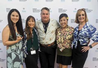 Four women and one man pose on a red carpet in front of a step-and-repeat emblazoned with the Hawaii International Film Festival logo.