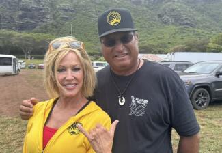 On the left, a person wearing a yellow sweatshirt throws a shaka. On the right is a person in a black T-shirt and black baseball cap.