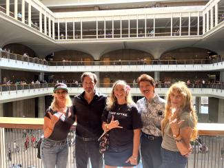 Five people dressed casually smile on the second floor of an atrium at the Hawaii Capitol.