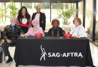 Six individuals sit and stand behind a black “SAG-AFTRA” tablecloth.