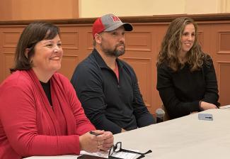 Panelists Jessica Maher in a red top, Aaron Kahl in a baseball cap and Ashley Skomurski in black sit at a table smiling.