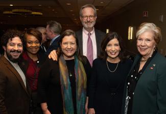 A group of six people smile in the ballroom of a hotel.