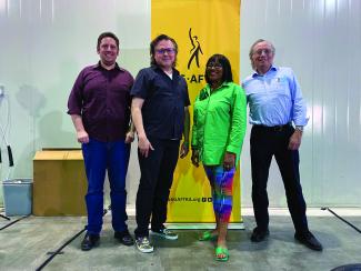 Four people stand in a room behind a standing yellow SAG-AFTRA banner.