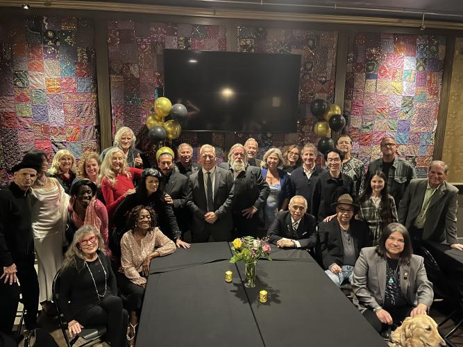 A group photo of a few dozen individuals dressed in formal and semi-formal attire stare at the camera.