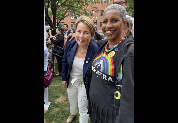 Healey wears white pants, a white top and a blue blazer, and stands next to Lyman who’s wearing a black SAG-AFTRA Pride T-shirt and rainbow necklace. 