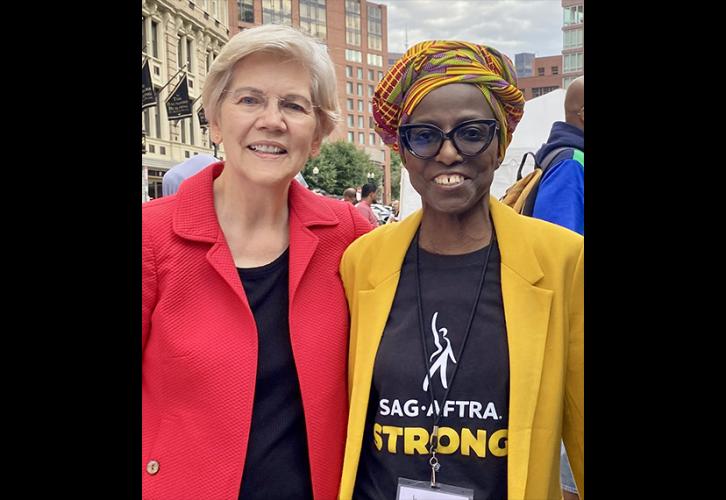 Warren wears a black top and red blazer and stands next to James in a colorful hair wrap wearing a yellow suit jacket, blank pants and a black “SAG-AFTRA Strong” T-shirt.