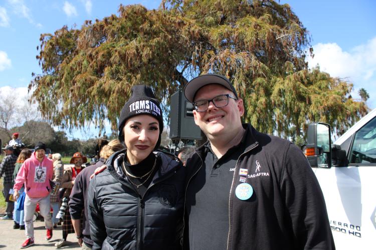 Dougherty, left, and Crabtree-Ireland stand closely for a photo. Both wear all-black outfits; Dougherty’s beanie bears “Teamsters” in all-caps; Crabtree-Ireland wears a fleece jacket with the SAG-AFTRA logo with pins and a large button. 