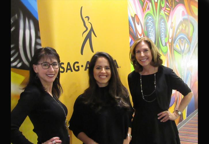 Three women in black dresses take a photo in front of the SAG-AFTRA banner.