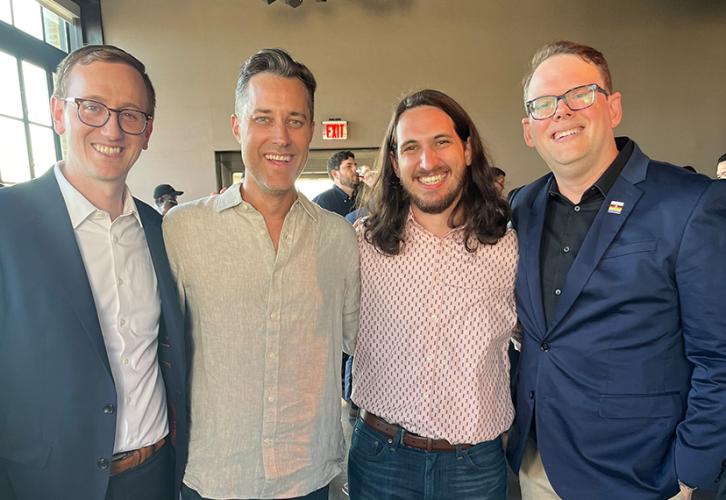 From left, Laadt, Talbert, Raskind and Crabtree-Ireland pose together. All are dressed in business casual attire. Also visible are other event attendees and, to the left, a window with natural lighting.