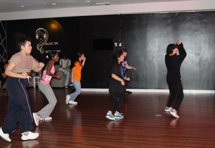 A group of individuals dance behind an individual leading them in a dance studio.