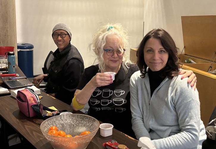 Three individuals sit at a table with snacks and drinks on the table.