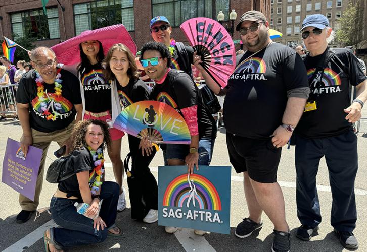 A diverse group of people on Boylston Street wearing SAG-AFTRA pride T-shirts holding rainbow fans and posters during the Boston Pride for the People Parade.