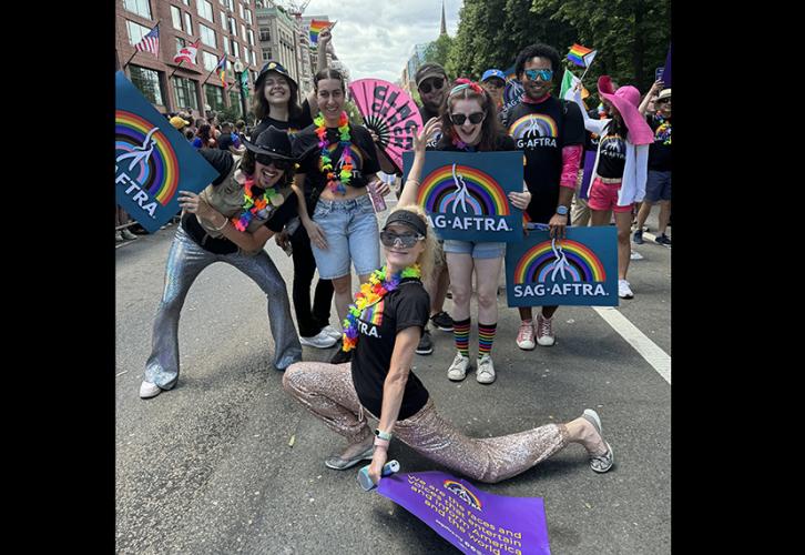 A diverse group of people wearing SAG-AFTRA pride T-shirts and leis hold LBGTQA+ signs, dance and cheer on Boylston Street during the Boston Pride for the People Parade.