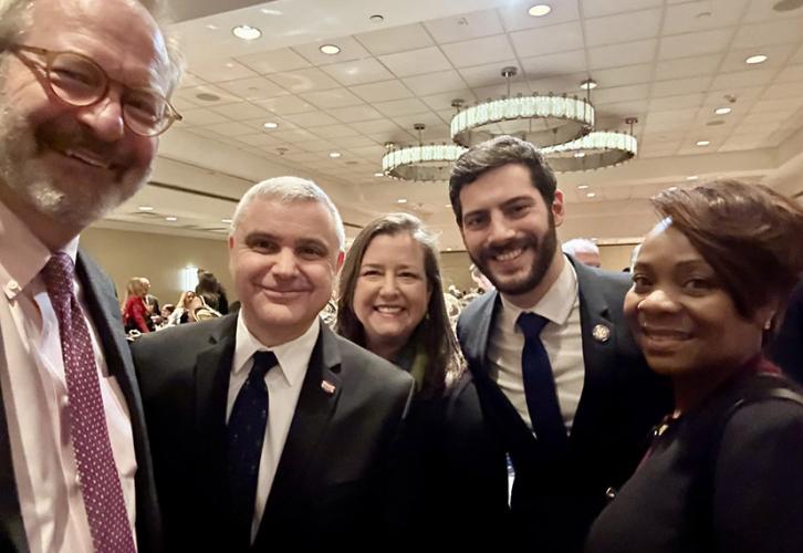 A group of five people are smiling. There are three chandeliers behind them.