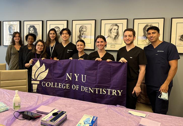 A group of people stand in a row holding a purple banner with white text that reads NYU College of Dentistry.