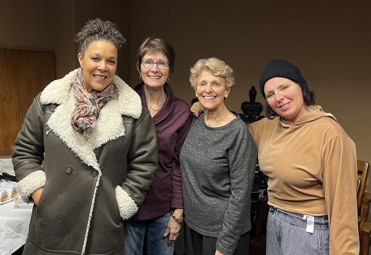 A diverse group of women smile for the camera in front of a tan wall