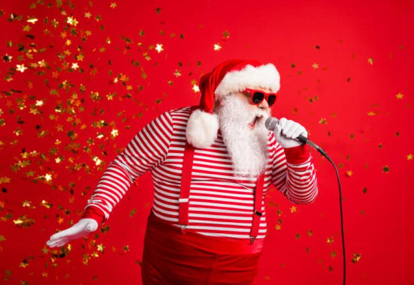 Man in white beard and red hat singing into a microphone