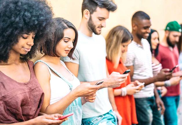 Image of teens standing against wall looking at cell phones