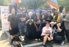 A diverse group of 19 people wearing a variety of SAG-AFTRA and IATSE T-shirts stand and kneel with an arch of white, blue and orange balloons in the background and a tall white banner on the left that reads in blue-and-orange letters, “It’s Better in a Union.” One of the people stands with his dog on a leash.