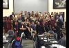 A diverse group of men and women stand for a photo in front of a projector screen.