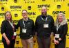 Four individuals on the red carpet in a nondescript room. Behind them is a yellow step-and-repeat backdrop with the SXSW logo. 