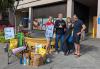 Four people stand in front of an office building loading dock with bags of donated food and a yellow banner with the words SAG-AFTRA in large black letters. The black SAG-AFTRA logo can also be seen on the banner behind the food.