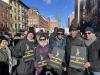 A group of diverse people dressed in winter coats hold black signs that read “SAG-AFTRA in Solidarity” in white and yellow text