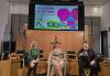 Three individuals sit in directors’ chairs with a colorful presentation behind them on a screen.