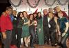 A diverse group of 13 SAG-AFTRA New England members pose for a photo in front of a SAG-AFTRA step-and-repeat decorated with a silver garland. Some sport holiday colors and hats.