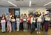 A group of people stand in a row holding pieces of art they have made out of canvas and multicolored pieces of paper.