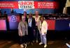 A group of five people stand in front of a stage with blue and red signs. A red banner stretches across the screen and reads “Constitutional Convention 2024. Better Wages, Better Benefits, Better Working Conditions. New York State AFL-CIO: Union Strong” in white text.