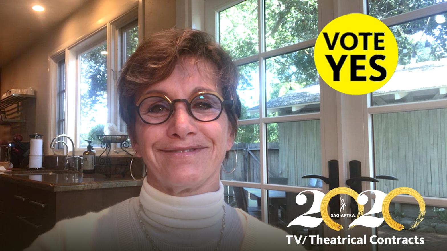 Carteris in white turtle neck and circle glasses in front of windows with a yellow "Vote YES" with black text in the top right corner and 2020 TV/Theatrical logo in bottom right corner